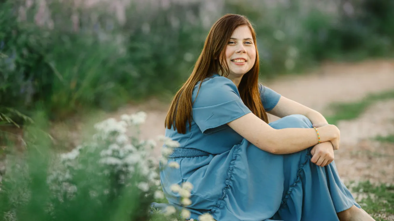 Morgan smiling, sitting outdoors among wildflowers