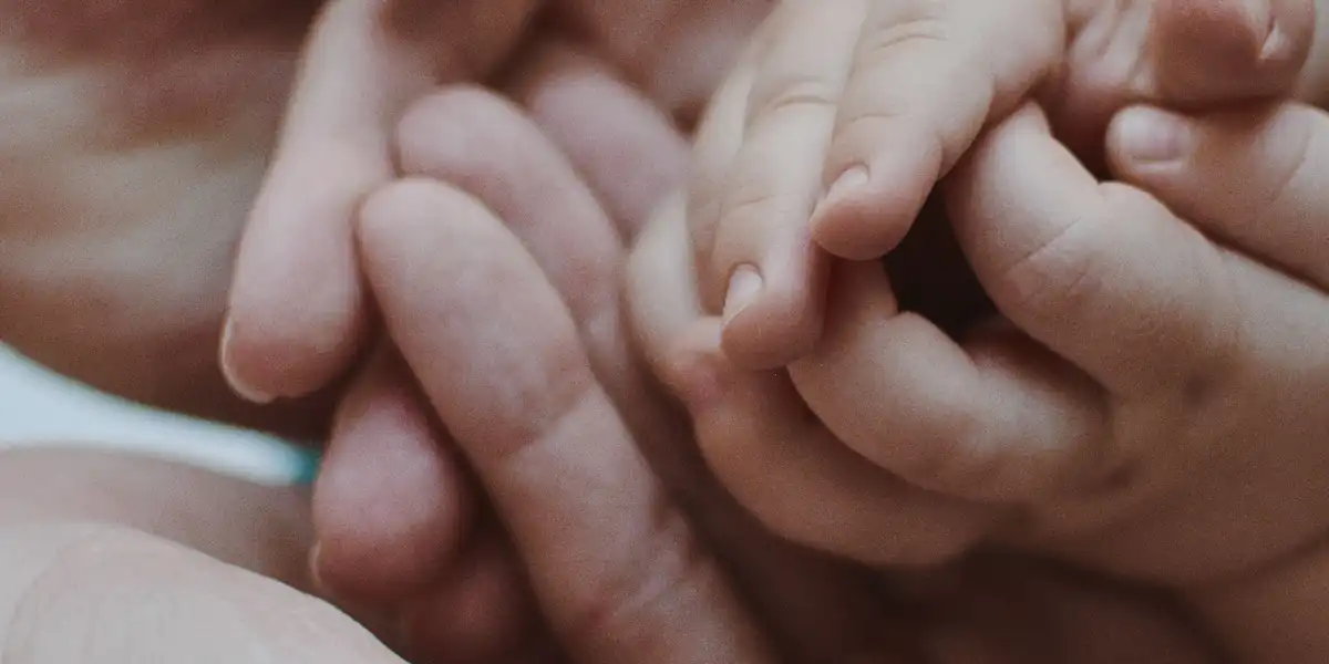 An adult hand gently holding a small child's hand