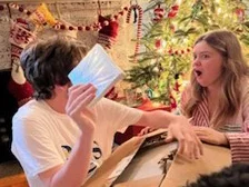 Two children opening a holiday gift in front of the Christmas tree